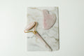 Rose quartz facial roller and jade gua sha stone flat lay on marble