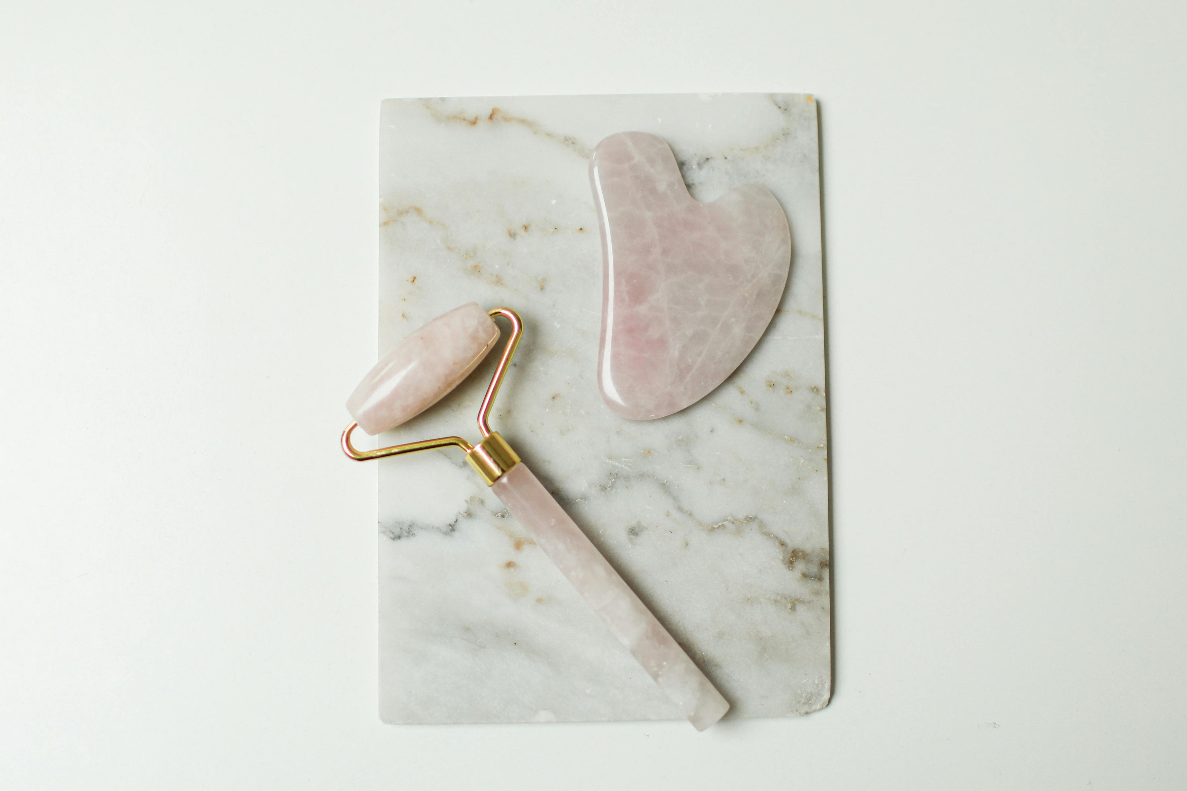 Rose quartz facial roller and jade gua sha stone flat lay on marble